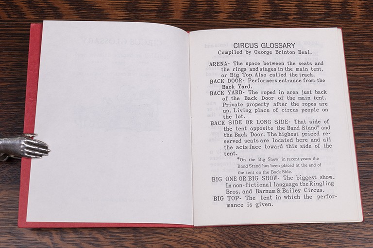 A small book is held open to a page showing definitions of words used at the circus.