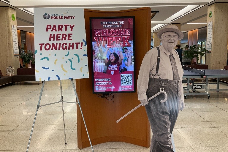 Herman B Wells cutout at the Wells Library next to a screen and a poster about the Wells party.