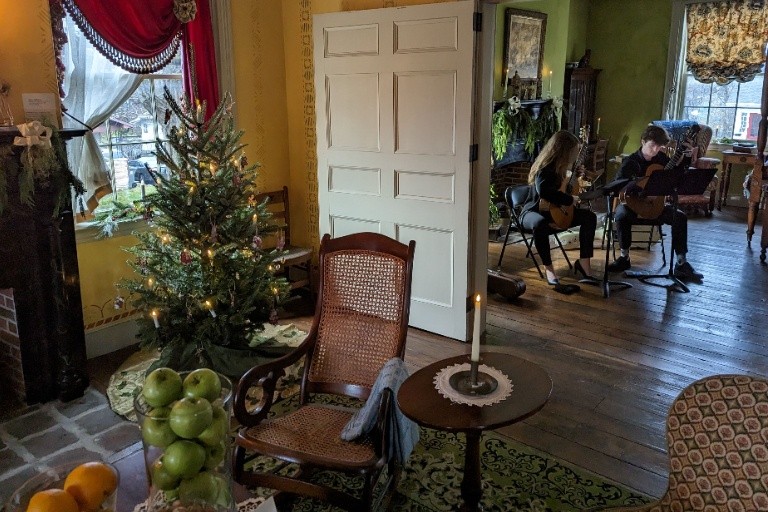 Interior room with rocking chair, christmas tree, and two seated people playing guitars