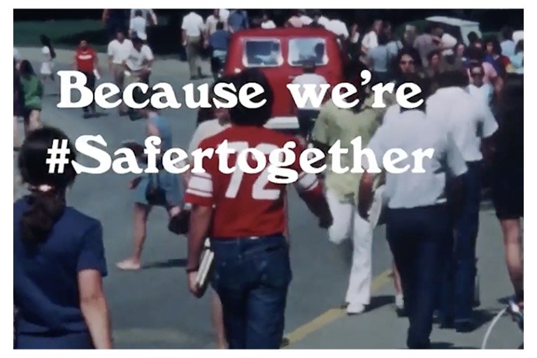 In the background, people walking in the street. In front of them, the words "Because we're #Safertogether".