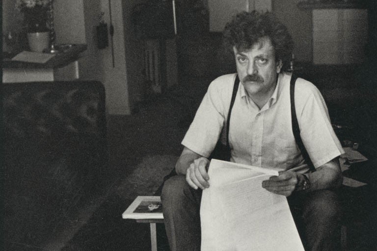 Kurt Vonnegut, seated, holding a sheet of paper