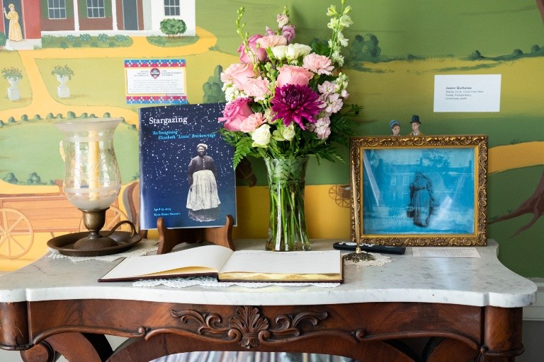 The Stargazing program is featured on the entryway table at the Wylie House Museum. Table has the "Stargazing" book, flowers, a framed picture, and an open book.