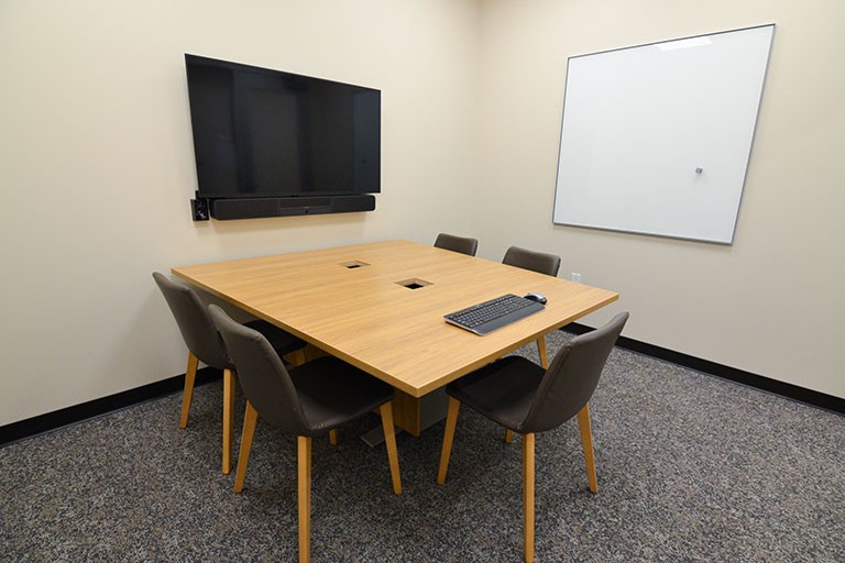 Photograph of a study room featuring a meeting table, chairs, computer keyboard, and monitor. 