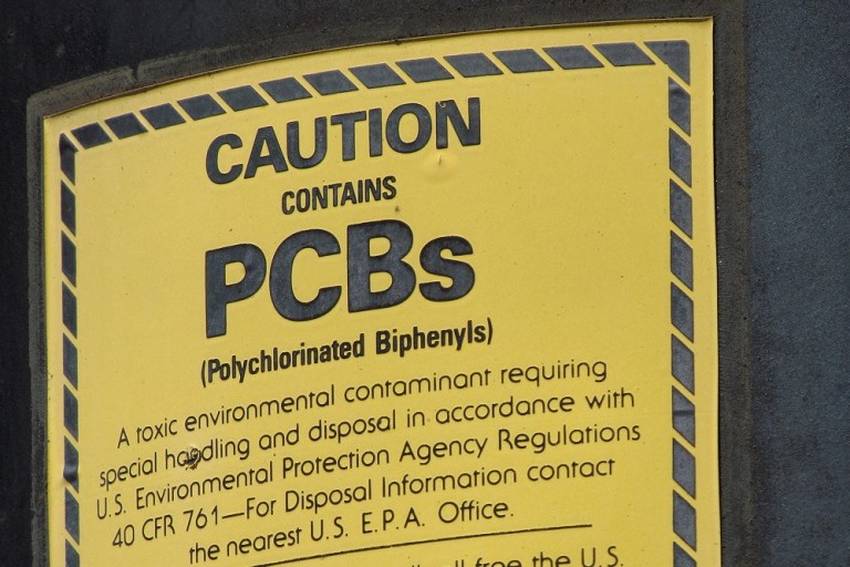 A yellow label with a black border warns against the presence of PCBs in an electrical transformer.