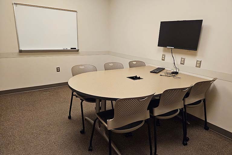 Color photograph of a study room with a table, six chairs, and a white board and monitor on the wall.