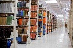 Rows of colorful books in tall shelving units line an aisle in an upper floor of the Wells Library stacks.