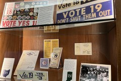 A photo of an exhibition display case featuring vintage posters proclaiming voting rights for 18 and 19 year olds