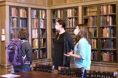 Three people stand in front of bookshelves inside the Lilly Library Ellison Room. All wear masks as one explains the history of the room.