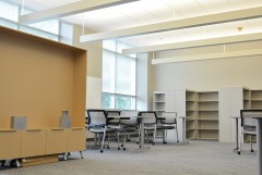 A room full of natural light has empty bookshelves surrounding new tables and chairs arranged as a library work space