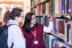 A library worker helps a student locate a book on the shelf.