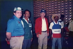 Four men standing in a row. Third from left is Richard Lugar. The man second from left wears a vest with a logo that has the letters PDC and a stylized fish logo. The man on the right wears a red, white, and blue shirt that reads "Vigilante."