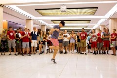 A large group of cheering students surrounds a student dancing in the Wells Library lobby.