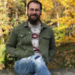Young man in beard and glasses smiles at the camera. Yellow leaves are behind him. It's a lovely Autumn day.