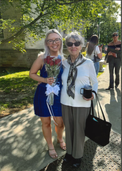A young woman in blue with flowers stands lovingly next to an older woman with glasses.