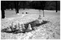 A snowy field, in which someone has cleared a rectangular space and built two rows of snowmen facing a snowman "professor" sitting at a snow desk.