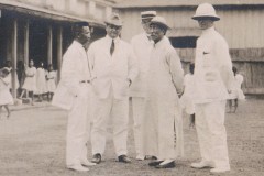 Five men in white suits and hats, standing outdoors