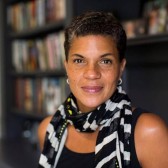 A headshot of Michelle Alexander posing in front of a blurred background of a bookcase