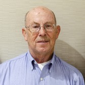 A photo of a man looking at the camera, wearing glasses and a button up shirt.